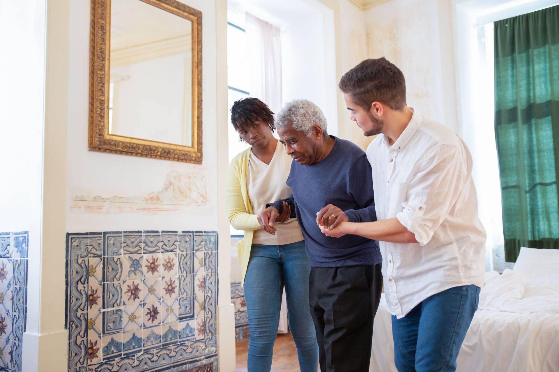 Three people examine a tiled bathroom wall beside a mirror and window.