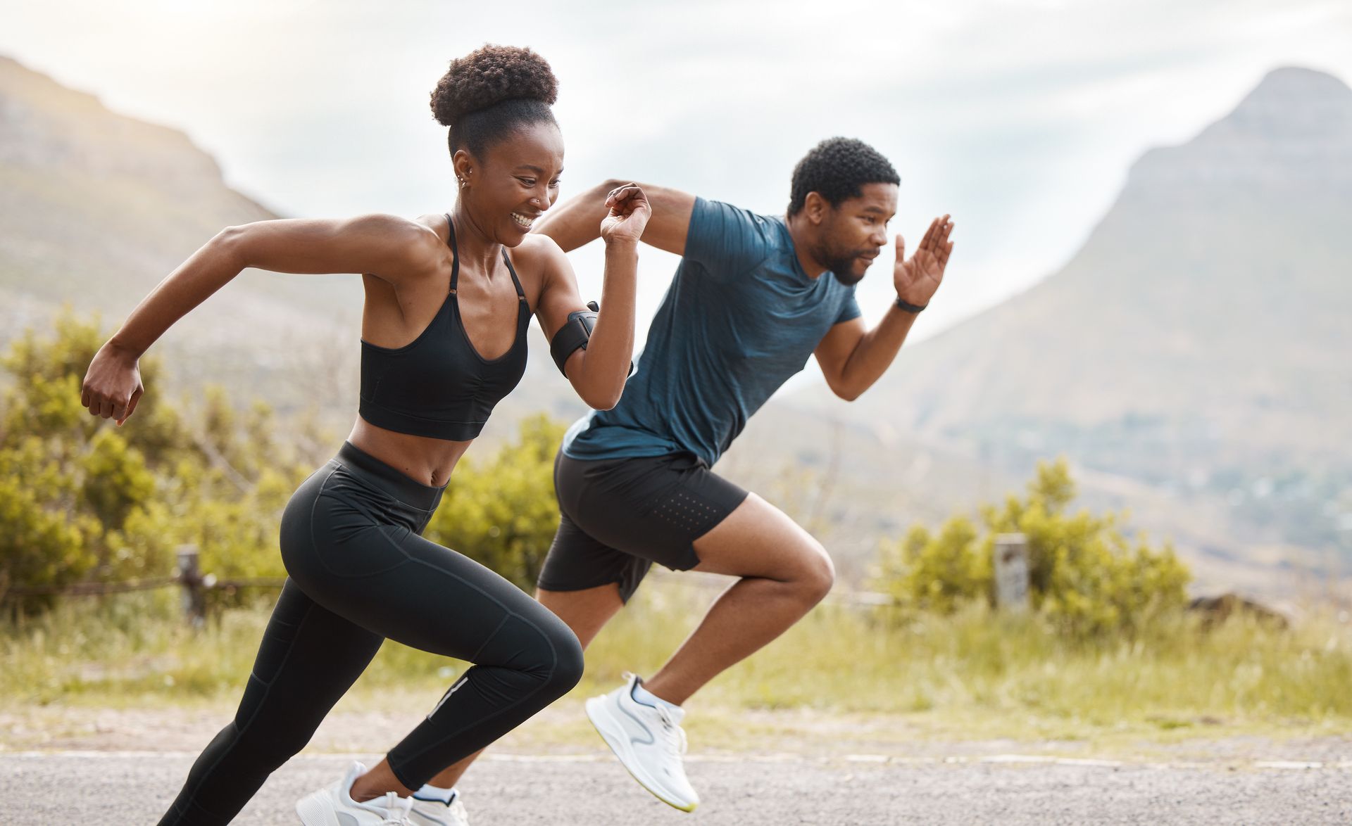 Two people running outdoors, smiling. Mountains in background.