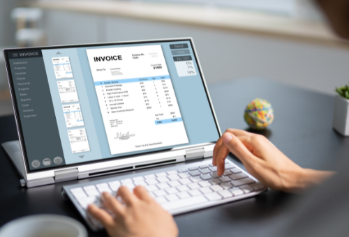 Person typing on a laptop displaying an invoice, likely at a desk.
