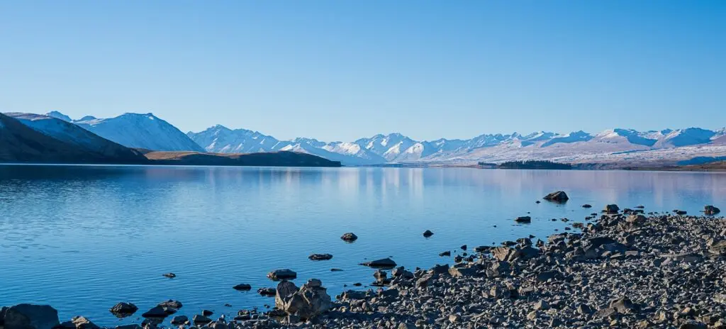 Coastal town with snow-capped mountains in the background, next to a tranquil bay.