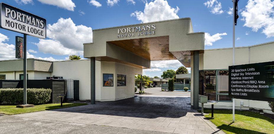 Hotel exterior with a blue roof, framed by tree branches, and a green lawn.