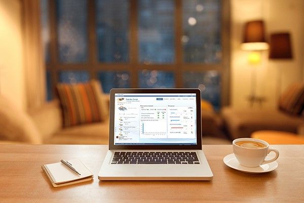 Laptop on a wooden desk with a notebook, pen, and coffee cup. Living room background.