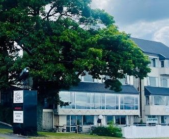 A building with a large tree in front of it; sign in front reads