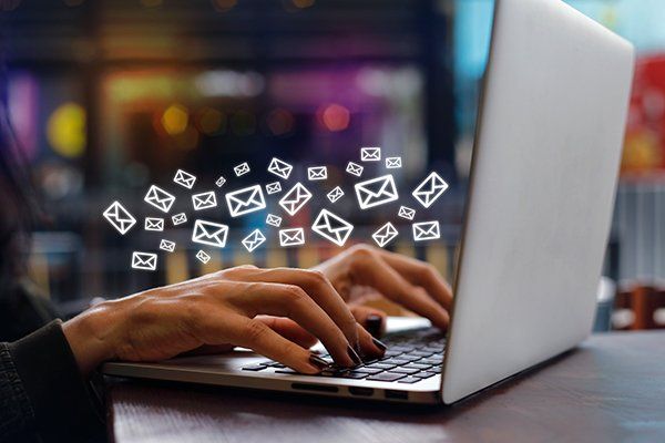 Hands typing on laptop, email icons floating above.