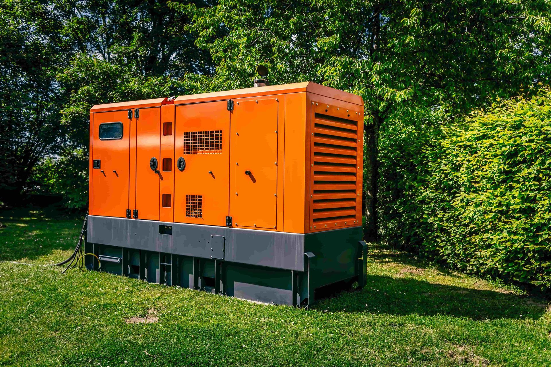 A large orange generator is sitting on top of a lush green field.