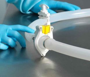 Hands in blue gloves, connecting white ventilation tubing with a yellow clasp, on a steel surface.