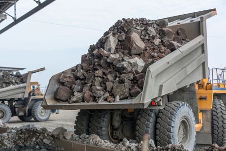 Mining industry heavy dump trucks unload granite into huge rock crusher
