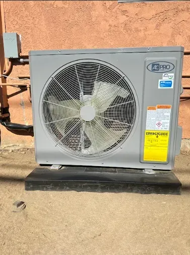 An outdoor AC unit, gray with a large fan, sits on a black platform near a building.