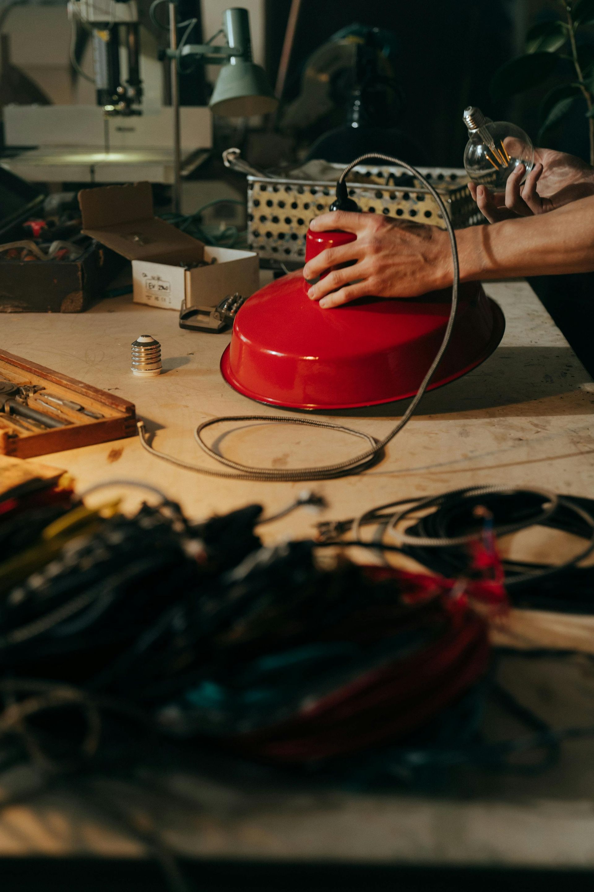 A person is working on a red lamp on a table.
