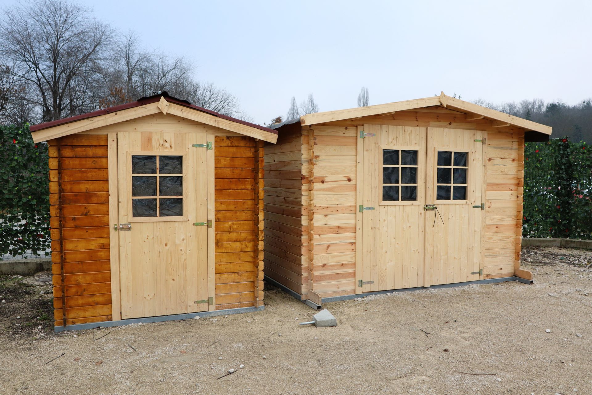 Two wooden sheds are sitting next to each other in a gravel area.