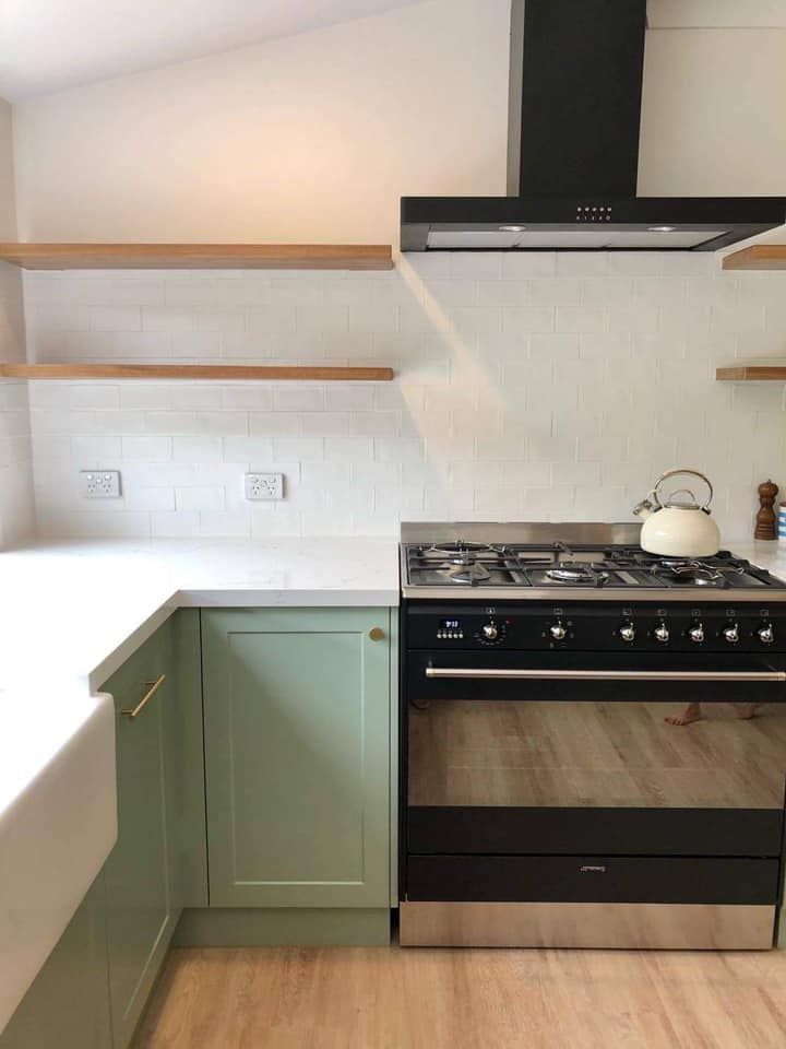 A kitchen with green cabinets and a black stove top oven.