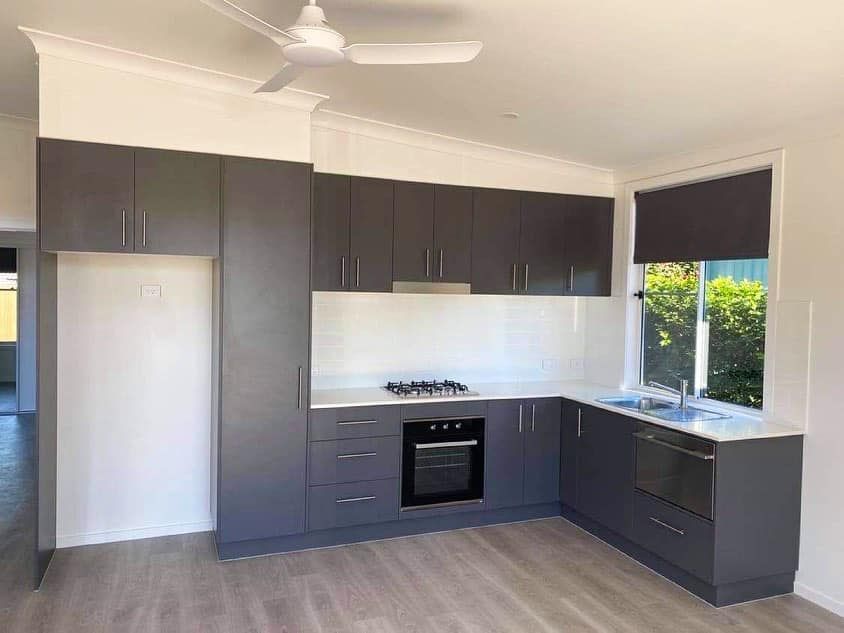 A kitchen with gray cabinets , a stove , a sink , and a ceiling fan.