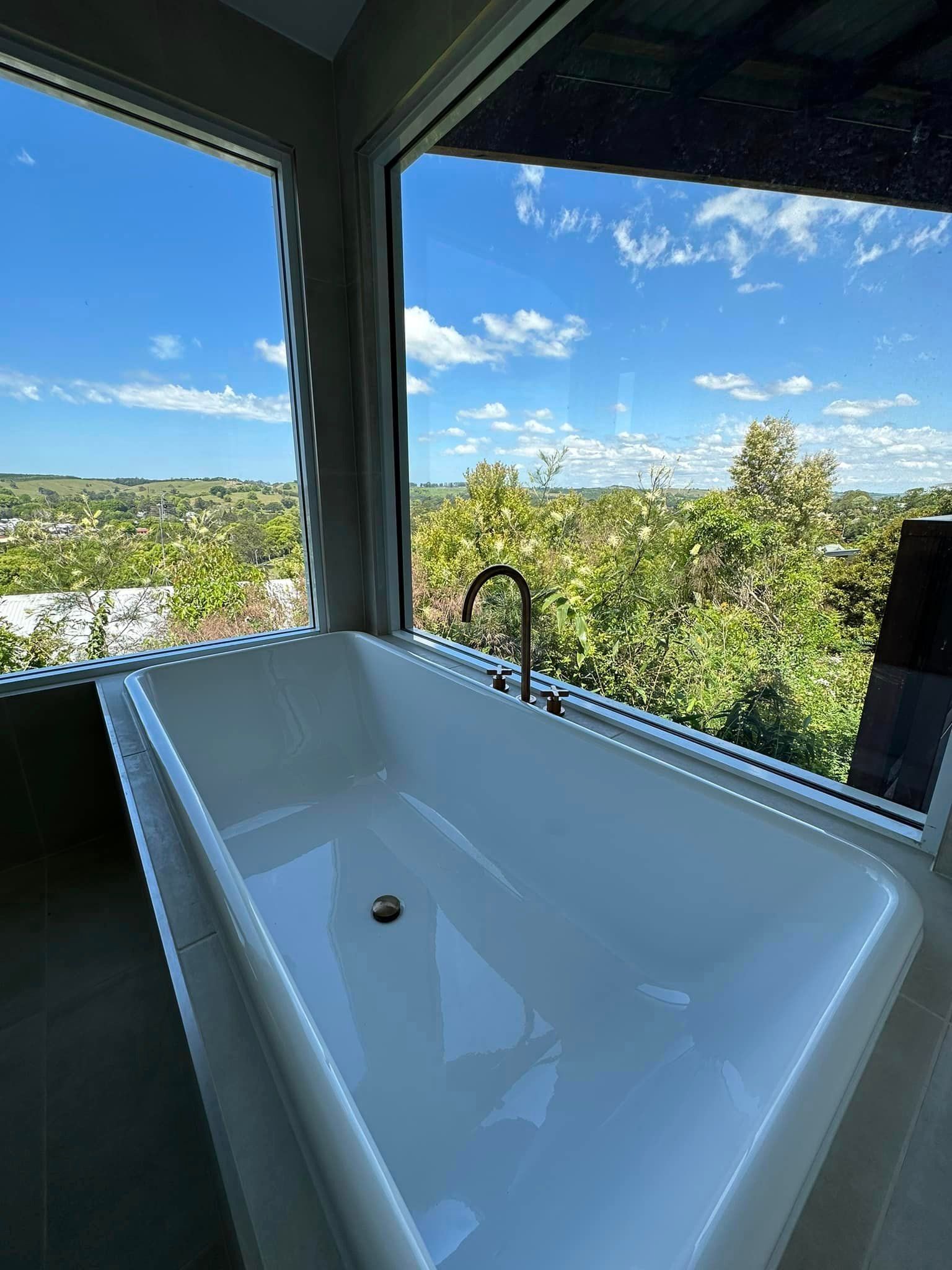 A bathtub in a bathroom next to a window with a view of trees.