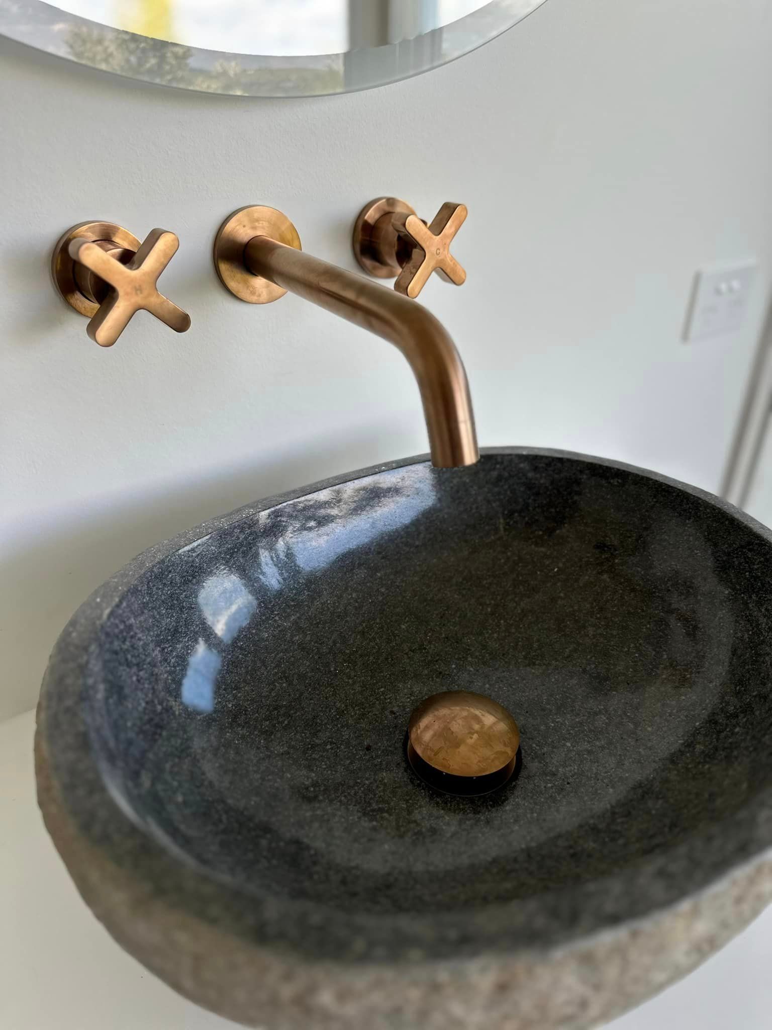 A bathroom sink with a copper faucet and a mirror.