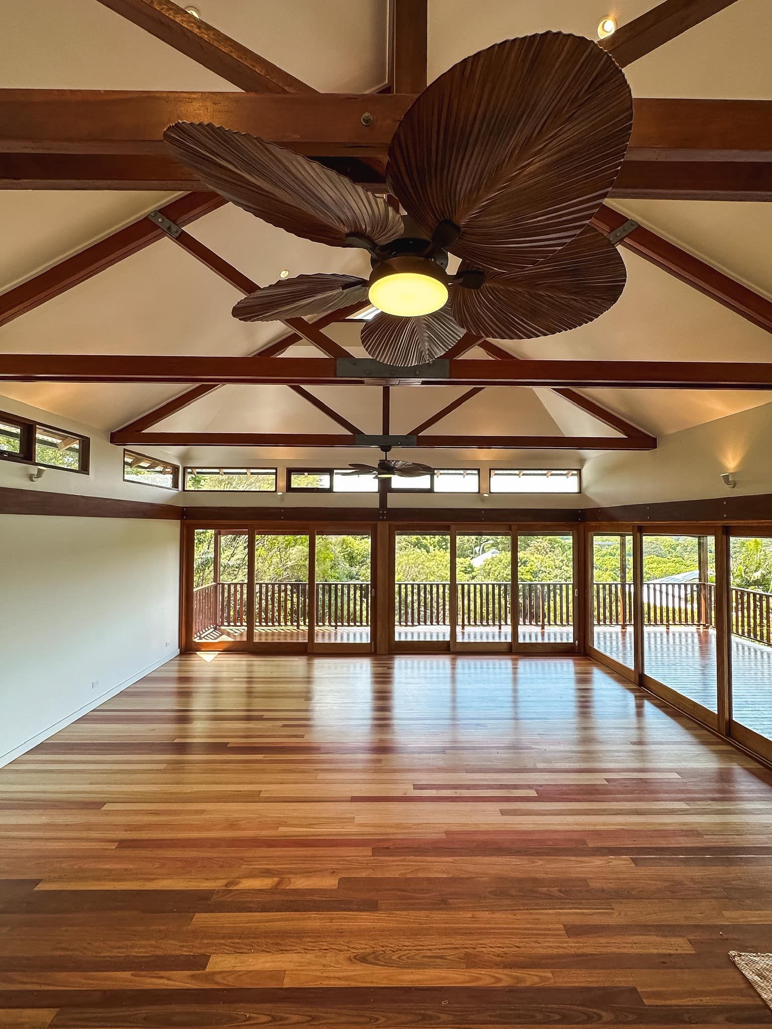 Open room with wood floors, ceiling beams, and large glass doors leading to a balcony. A ceiling fan is mounted overhead.