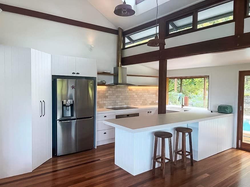 A kitchen with a stainless steel refrigerator , white cabinets , and wooden floors.
