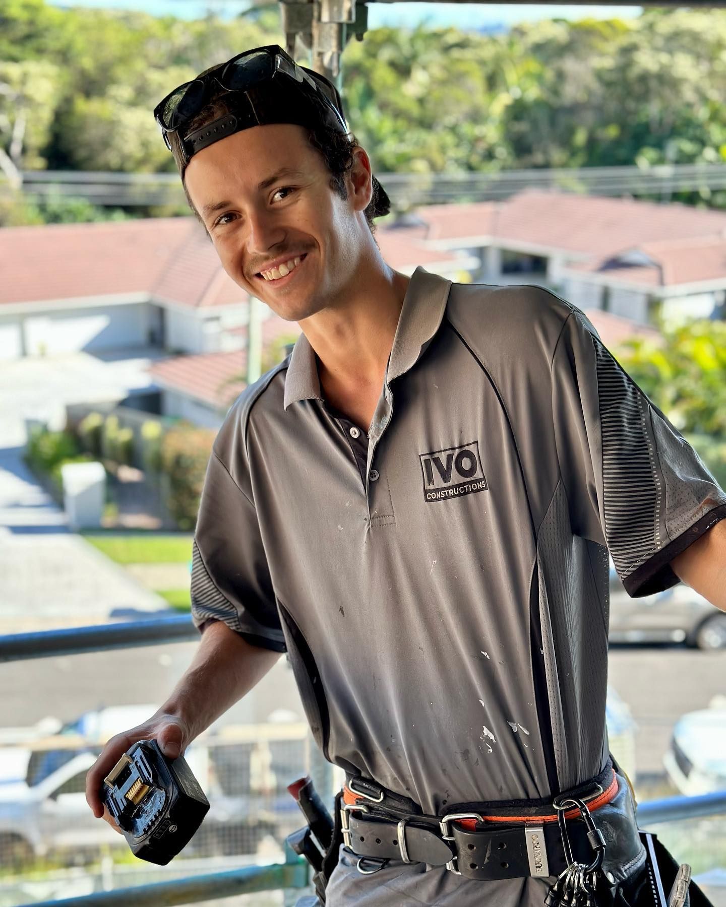 a man in a gray shirt is standing on a balcony holding a tape measure .