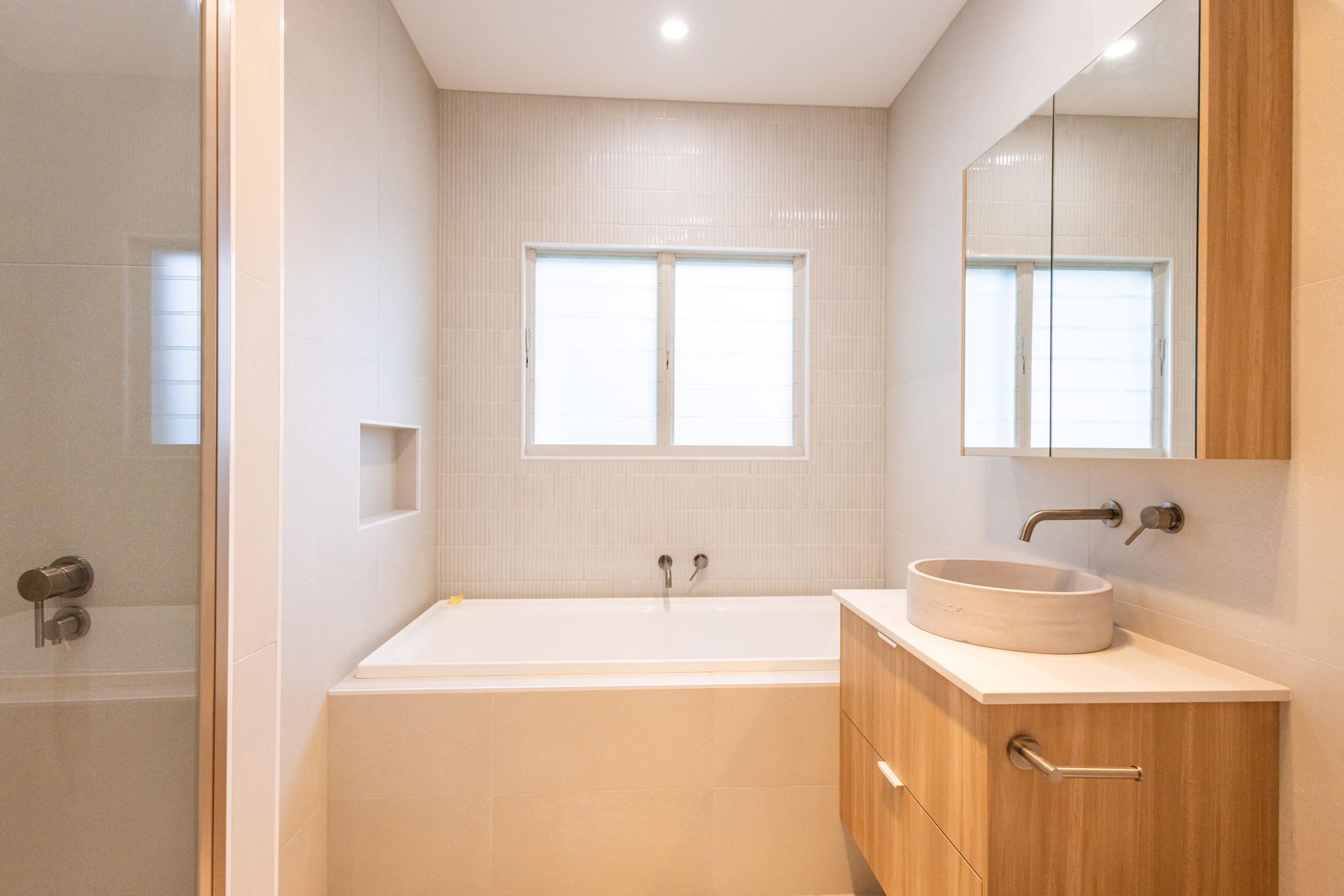 A bathroom with a tub , sink , mirror and window.
