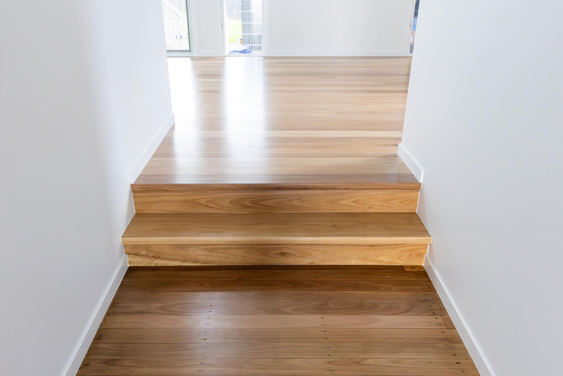 A hallway with wooden stairs leading up to a white wall.