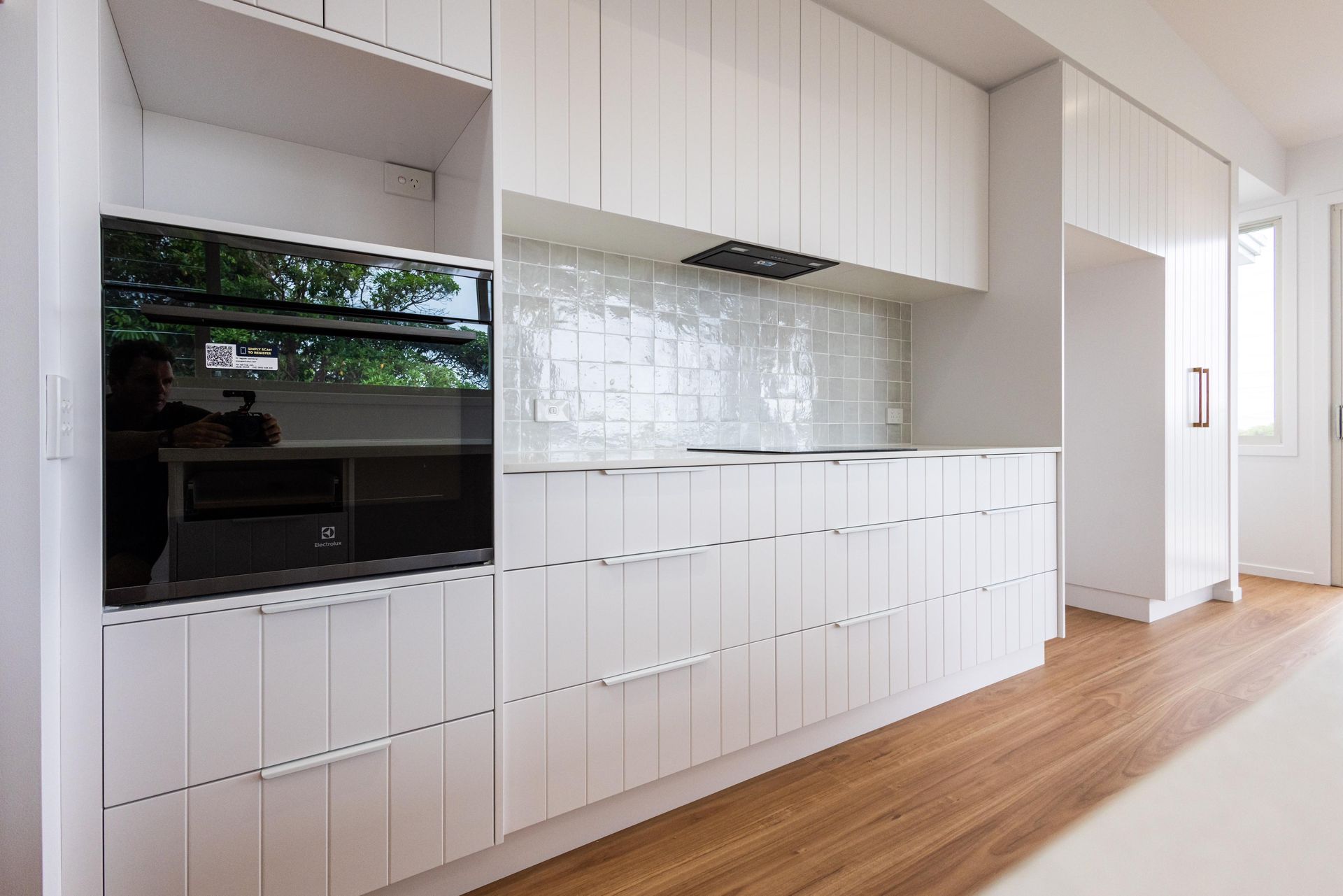 A kitchen with white cabinets , wooden floors , and a black oven.