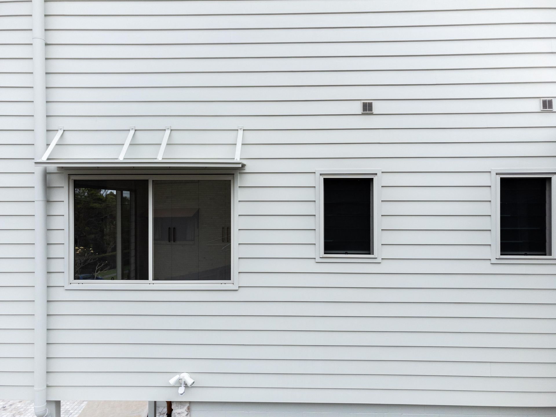 The back of a white house with two windows and a canopy.