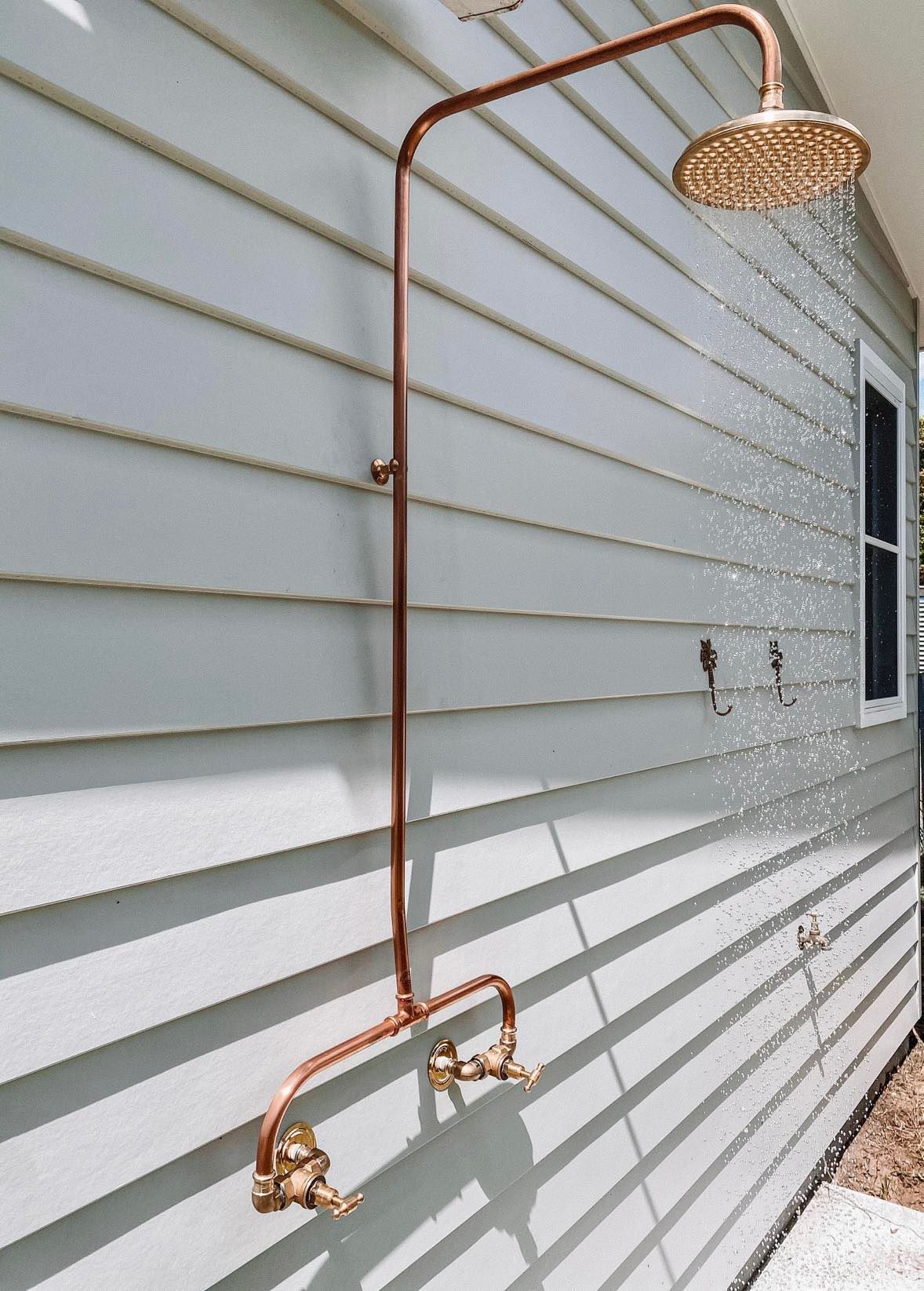 A copper shower head is attached to the side of a house.