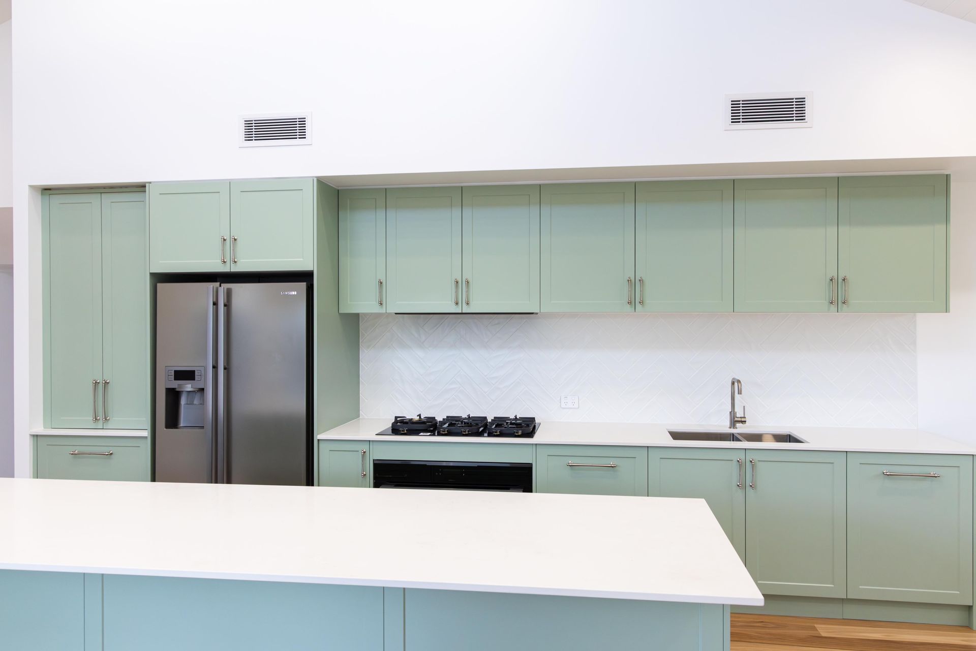 A kitchen with green cabinets and a stainless steel refrigerator