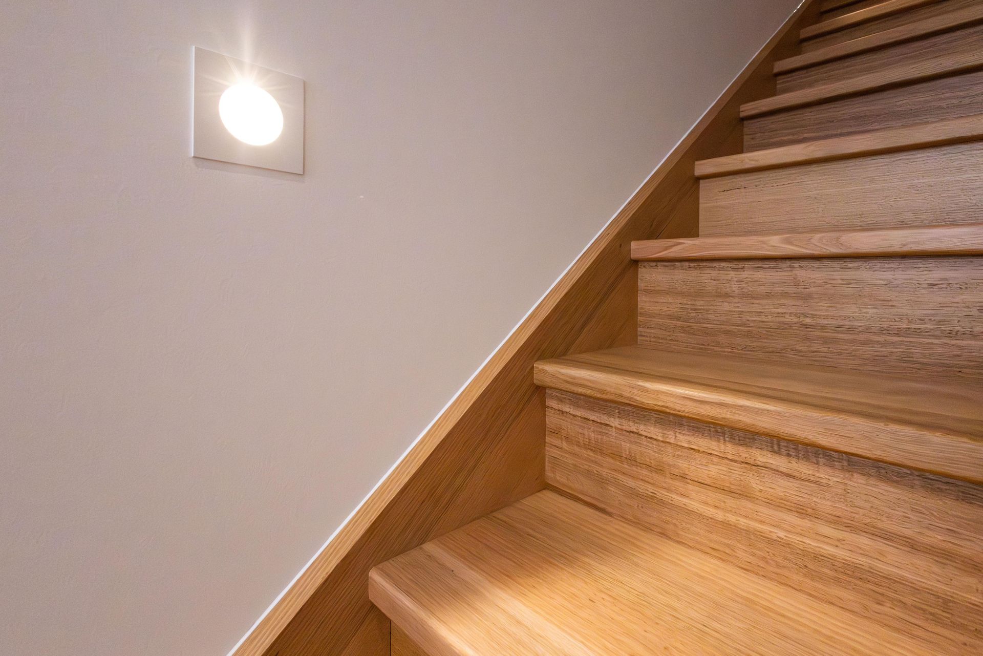 A close up of a wooden staircase with a light on the wall.