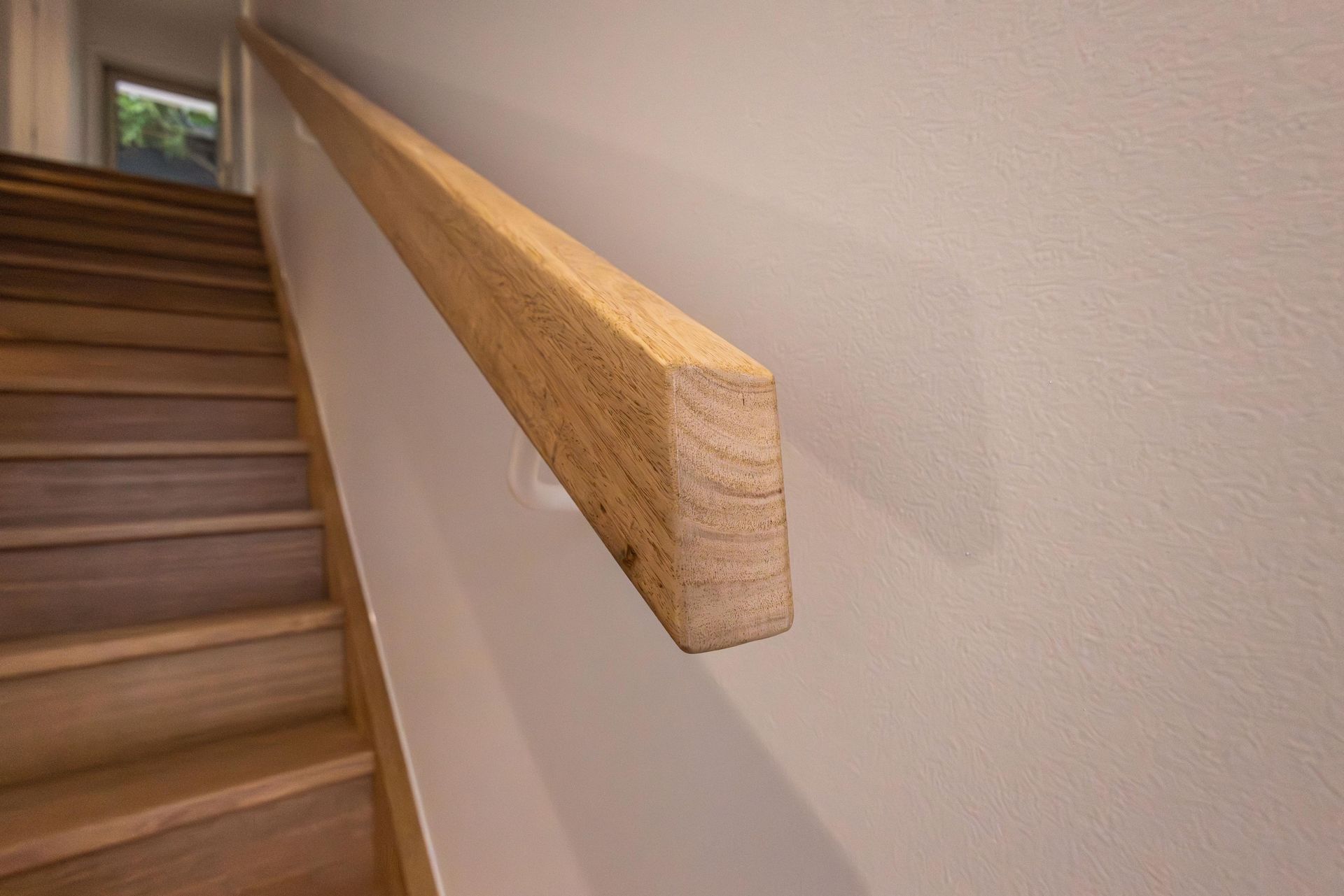 A wooden handrail is attached to a wall next to a set of stairs.