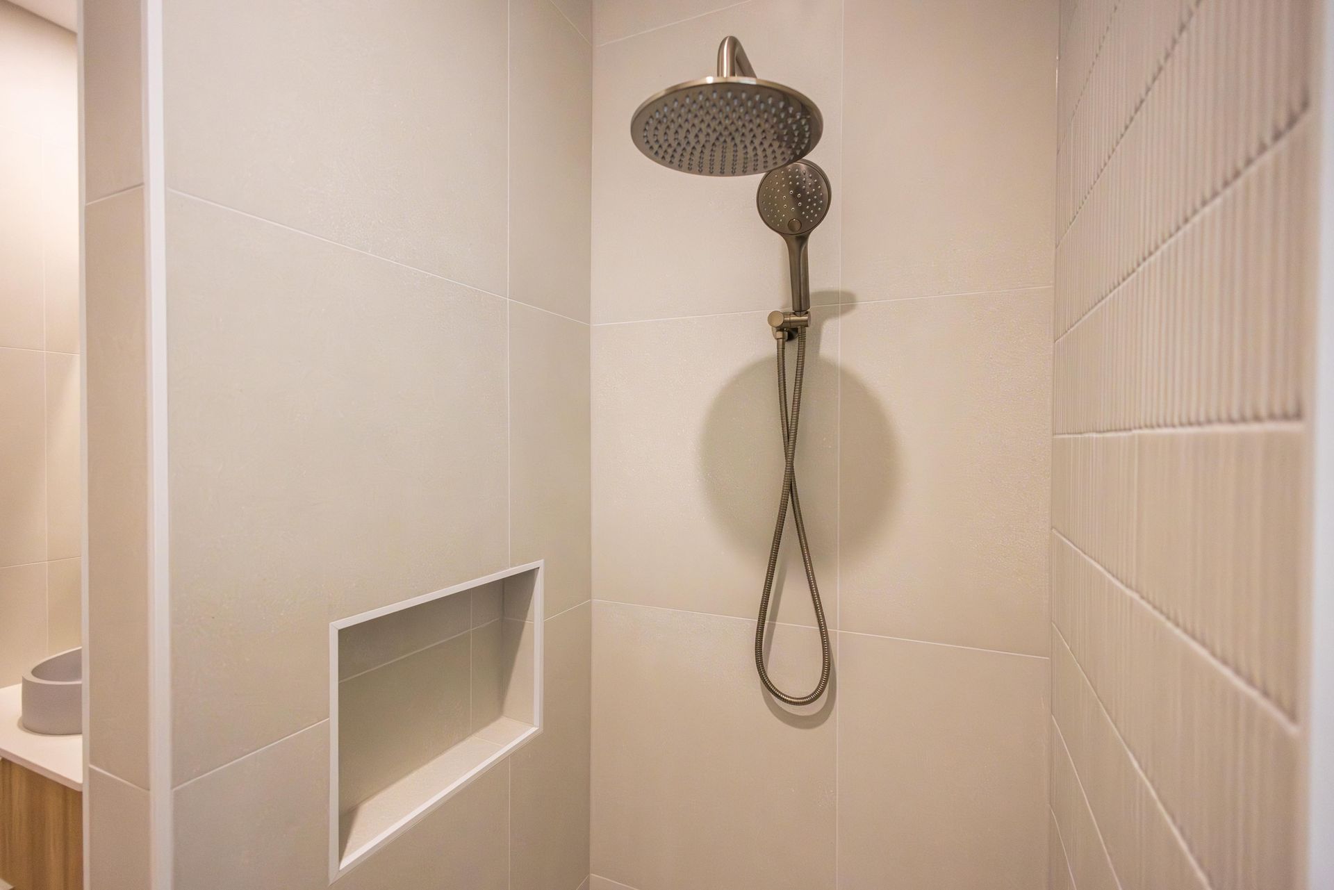A bathroom with a shower head and a shelf in the wall.
