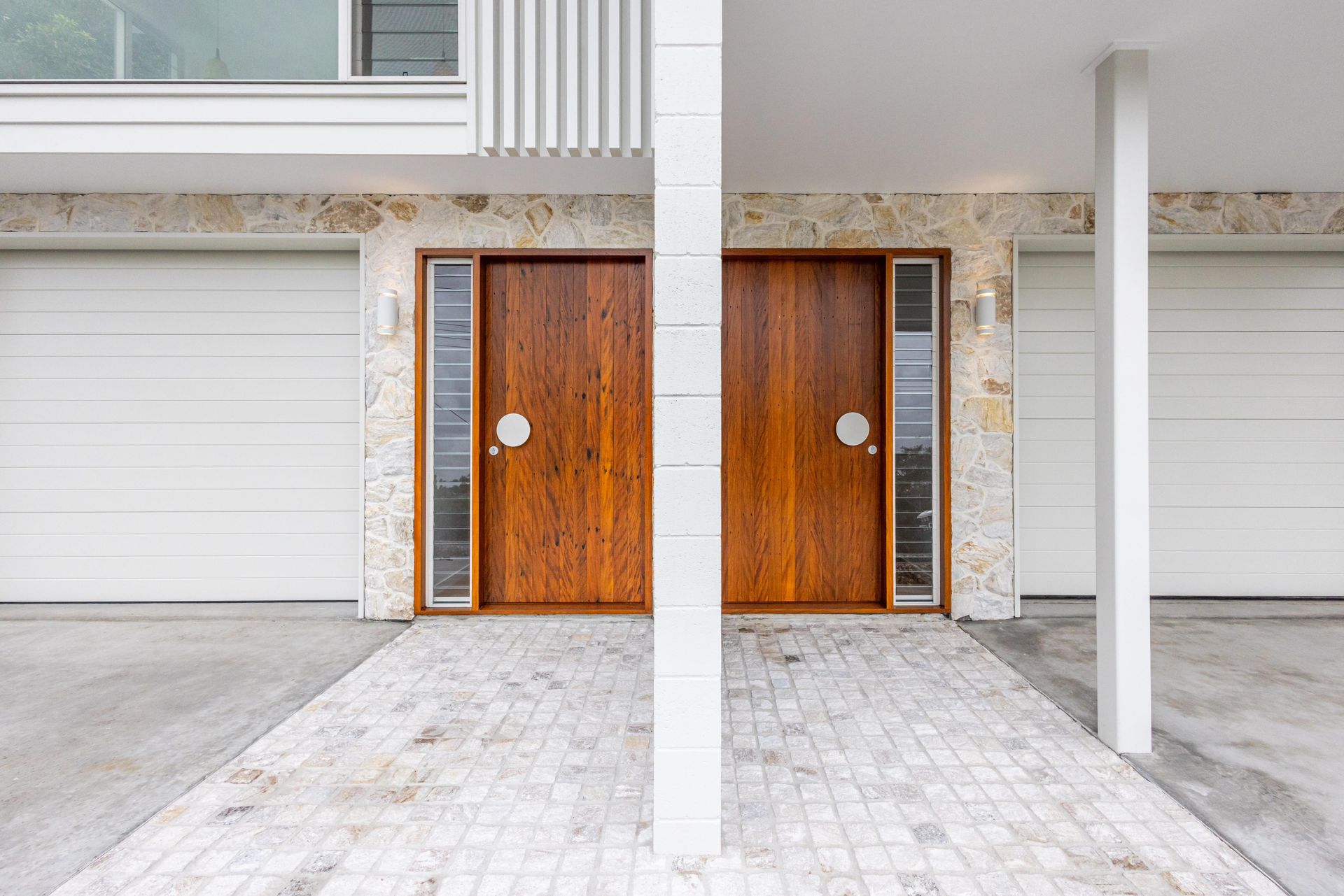 A house with two wooden doors and two white garage doors.