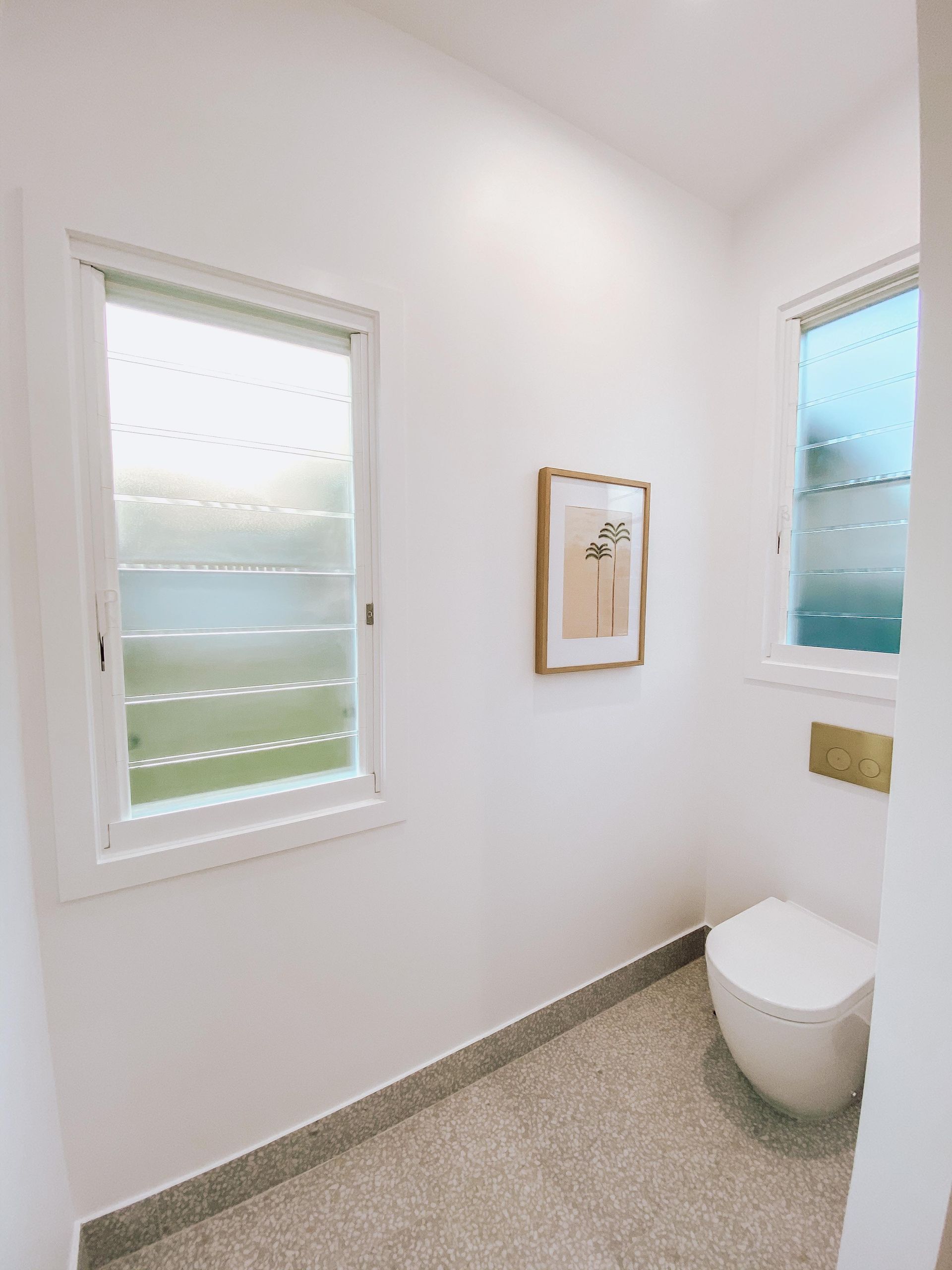 A bathroom with a toilet , window and picture on the wall.