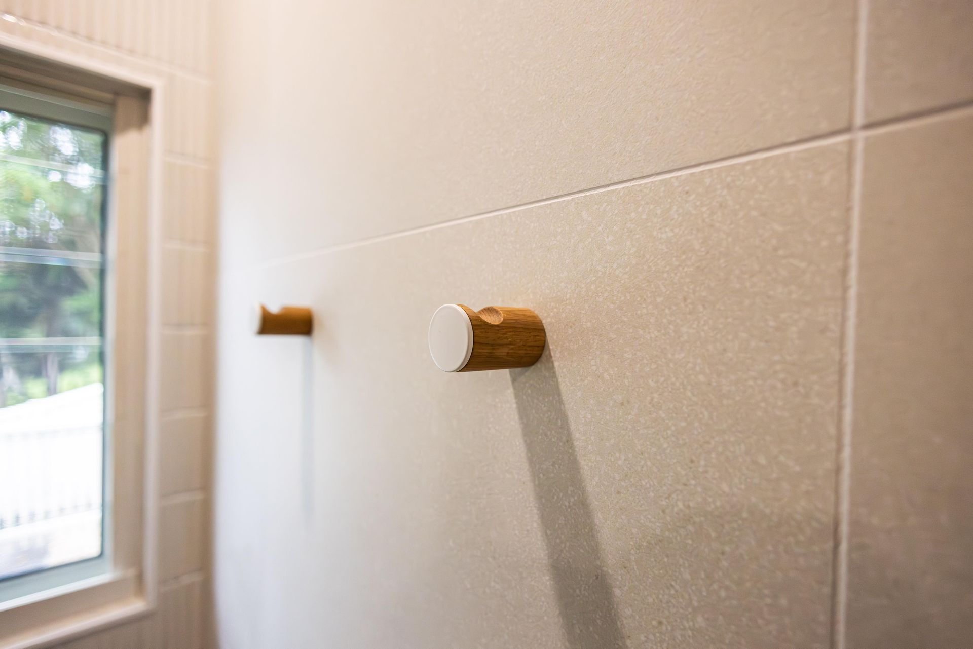 A bathroom with white tiles and wooden hooks on the wall.