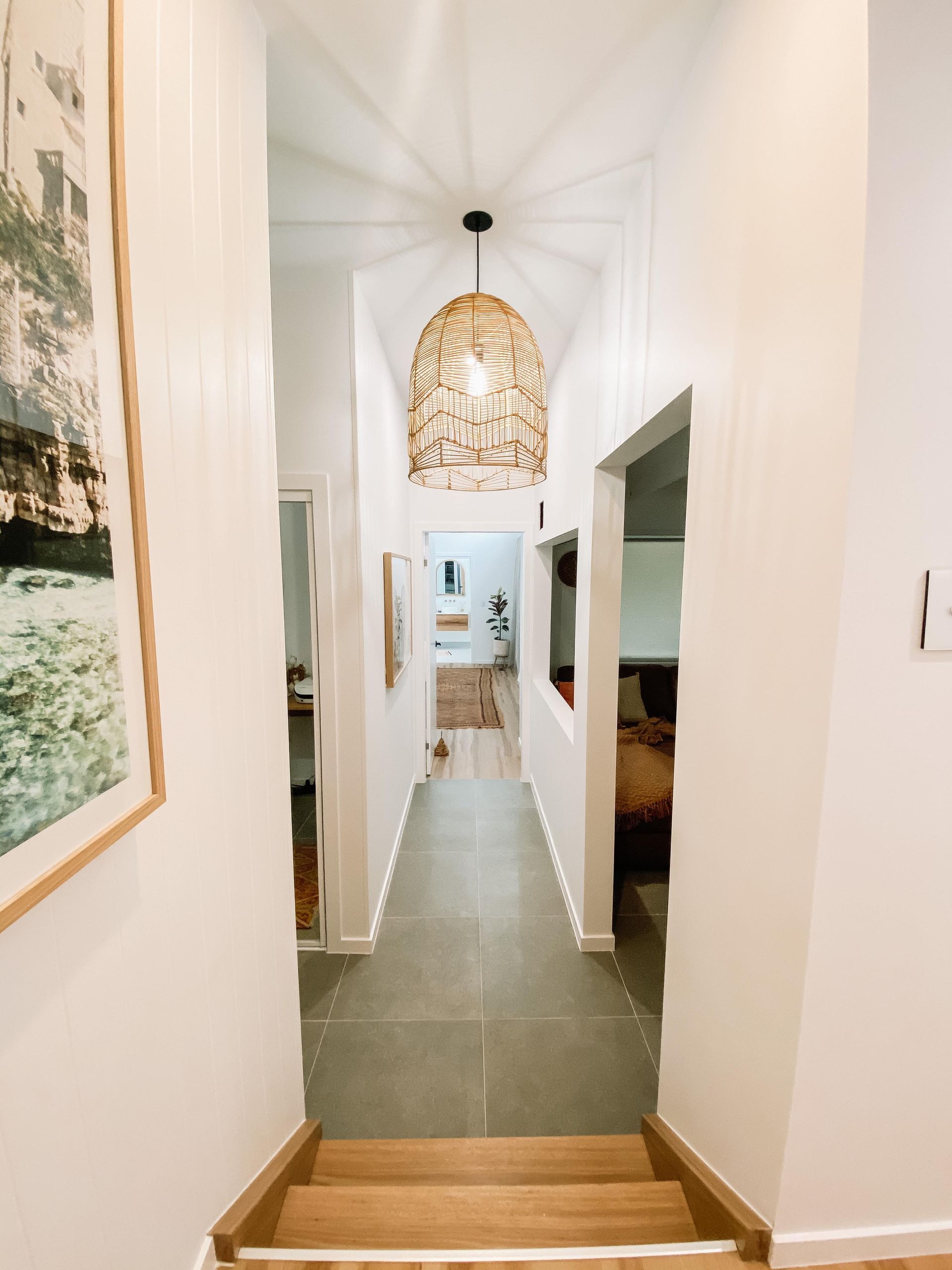 A hallway with stairs leading up to a living room and a picture on the wall.