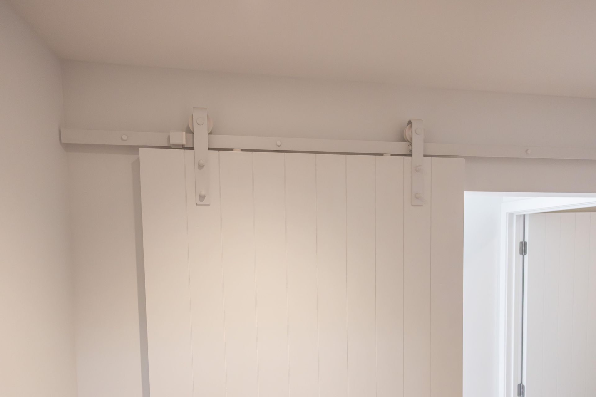 A white sliding barn door is hanging on a white wall next to a door.