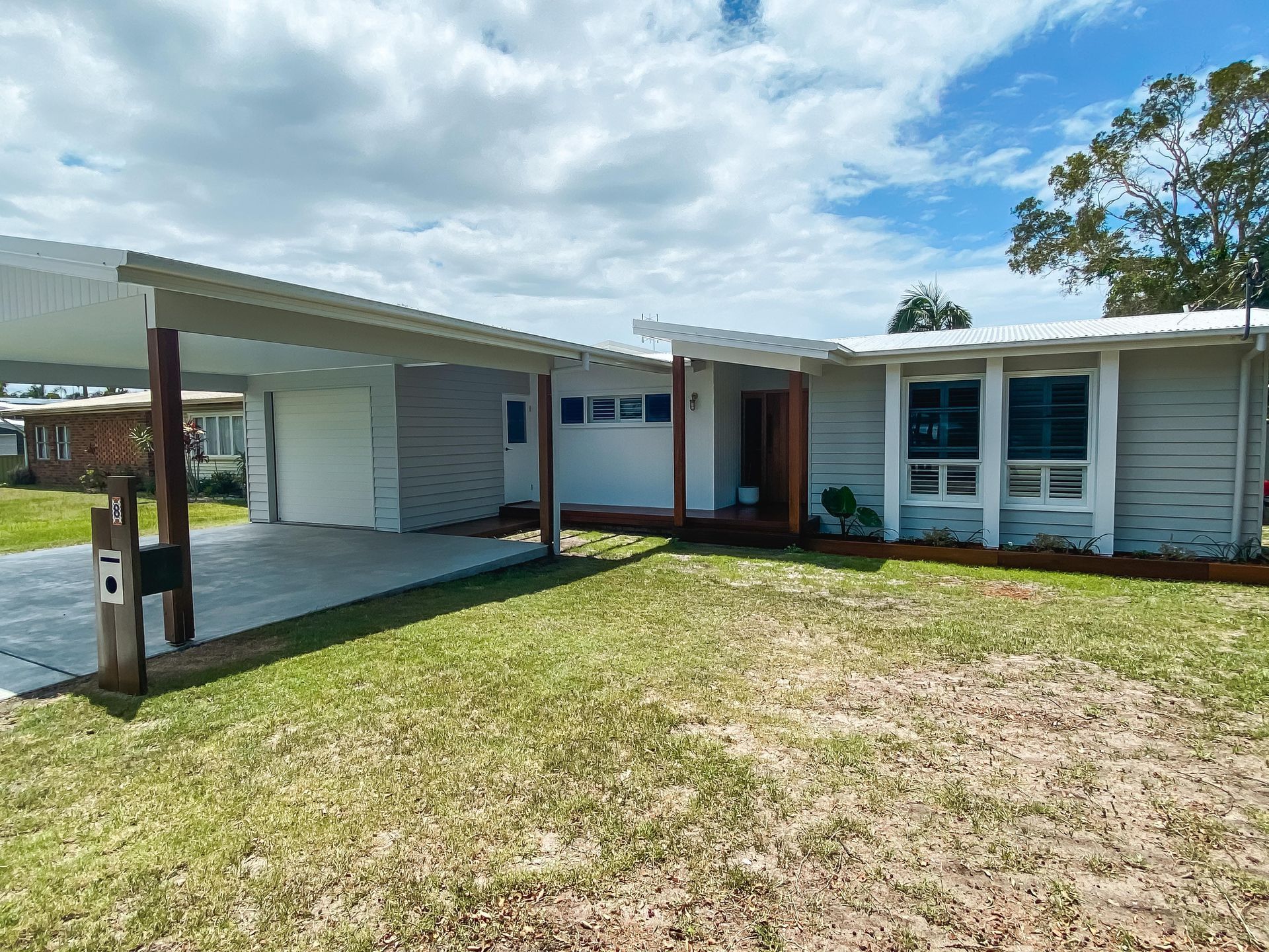 A white house with a carport and a large lawn in front of it.