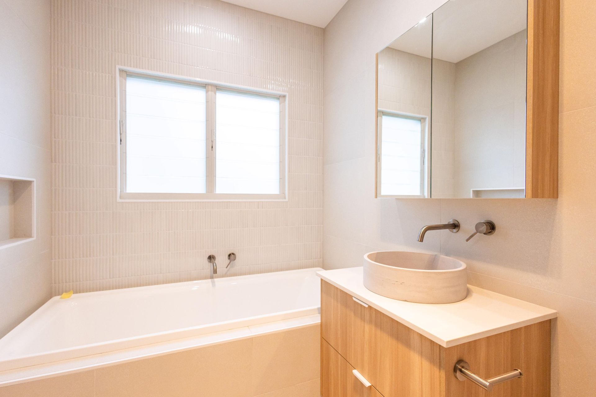 A bathroom with a tub , sink , mirror and window.