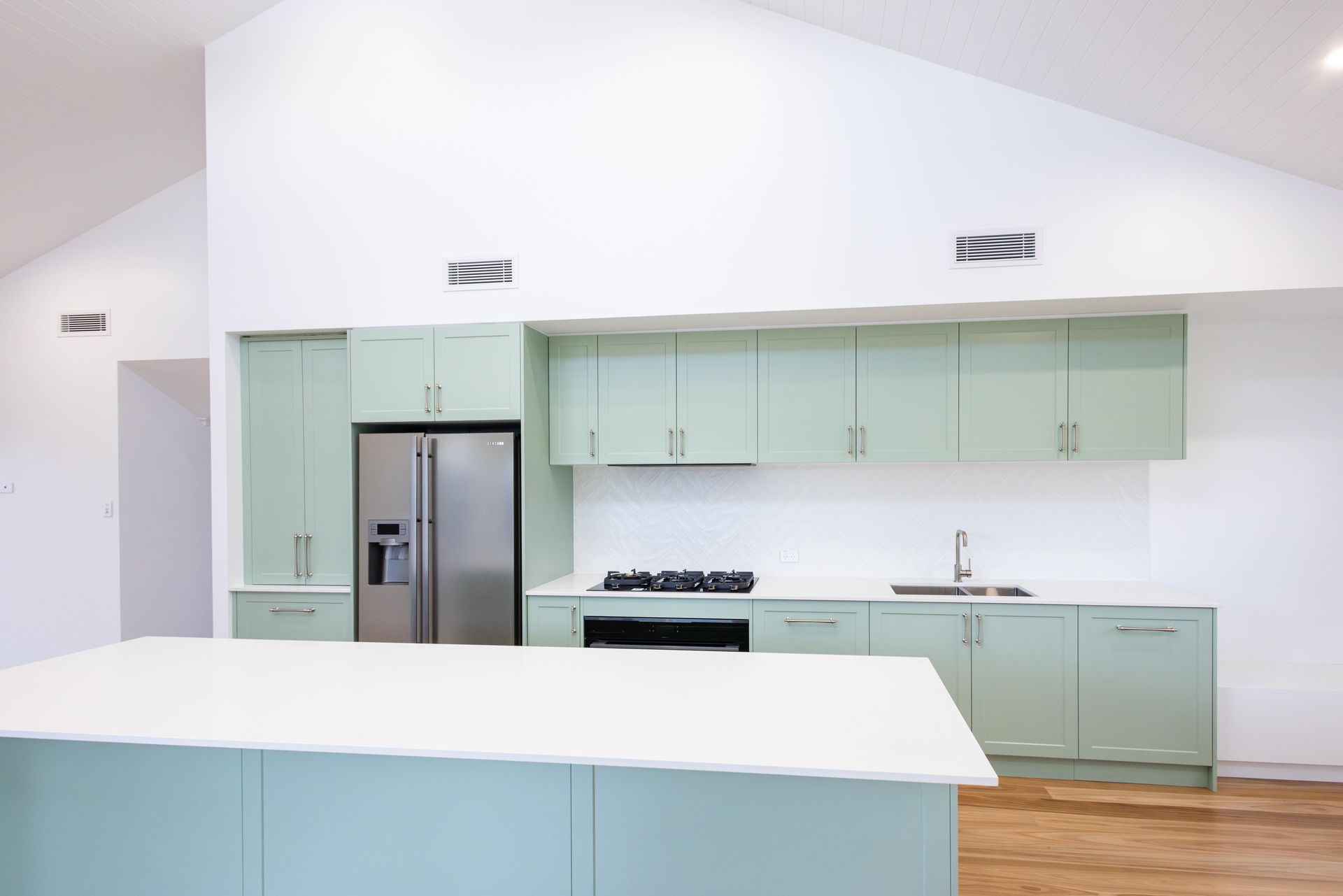 A kitchen with green cabinets and a stainless steel refrigerator.