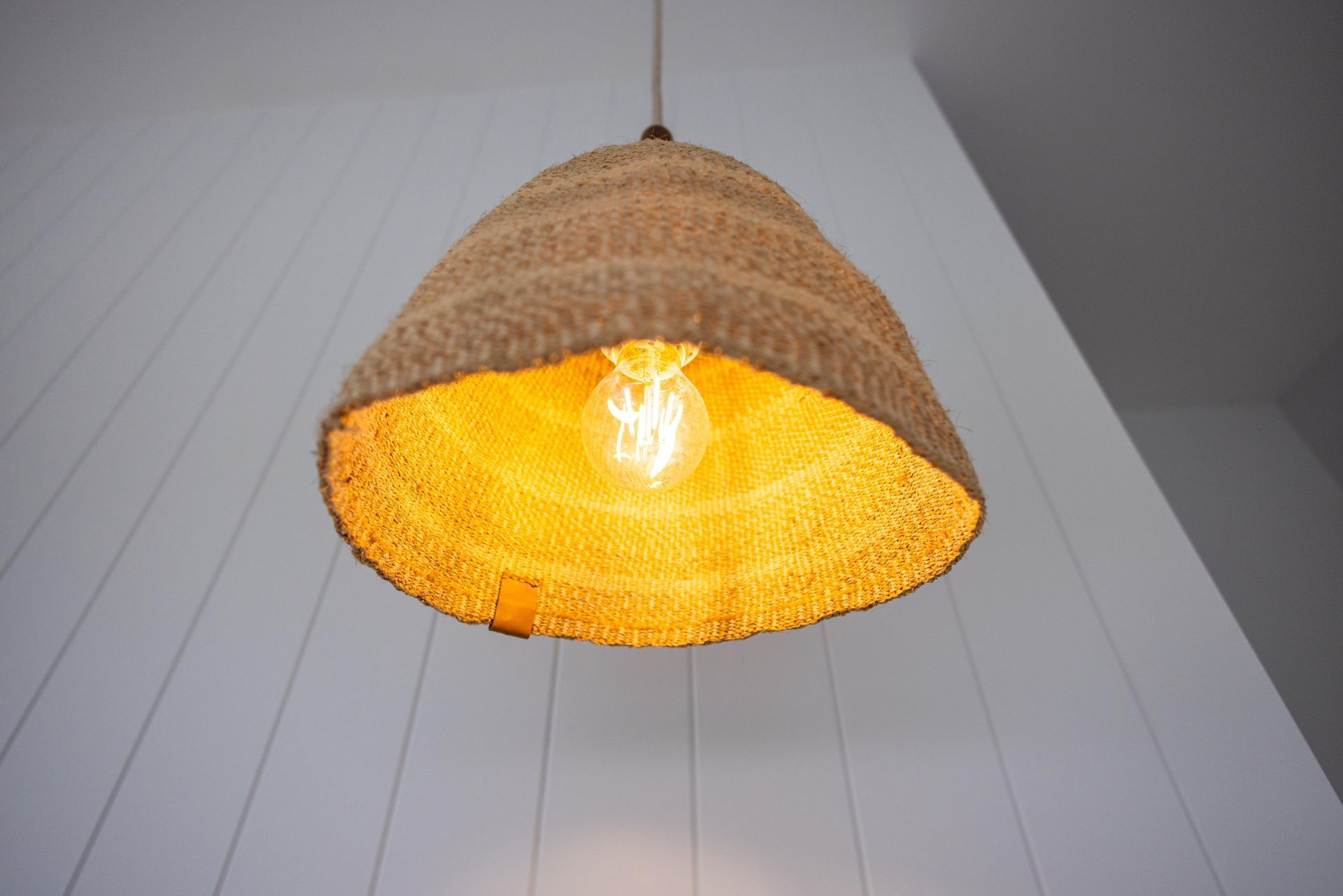 A wicker lamp hanging from the ceiling with a light inside of it.