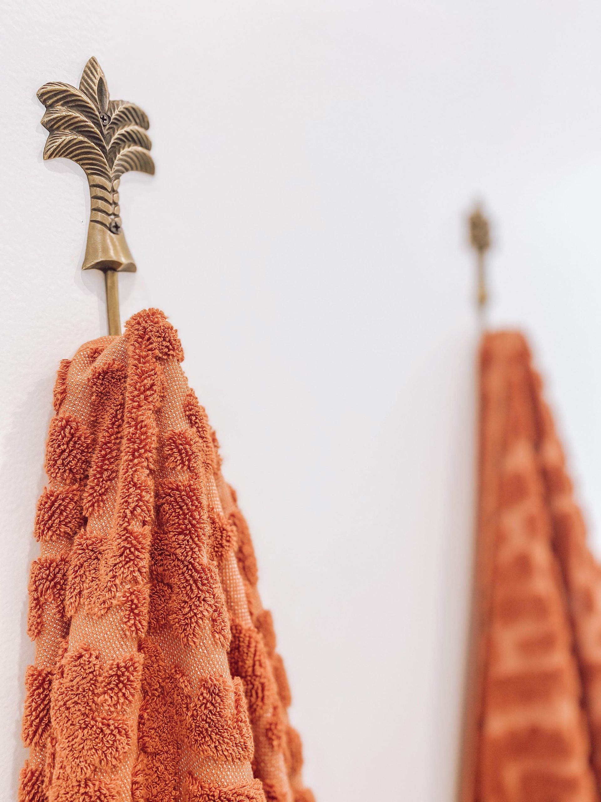 Two towels are hanging on a wall with a palm tree hook.