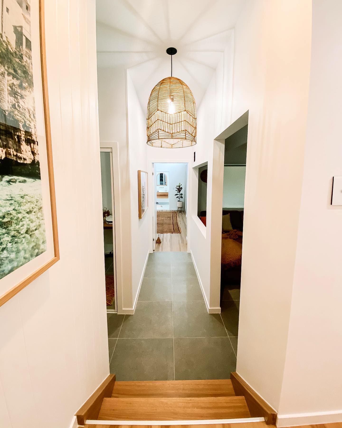 A hallway with stairs leading up to a bathroom and a picture on the wall.