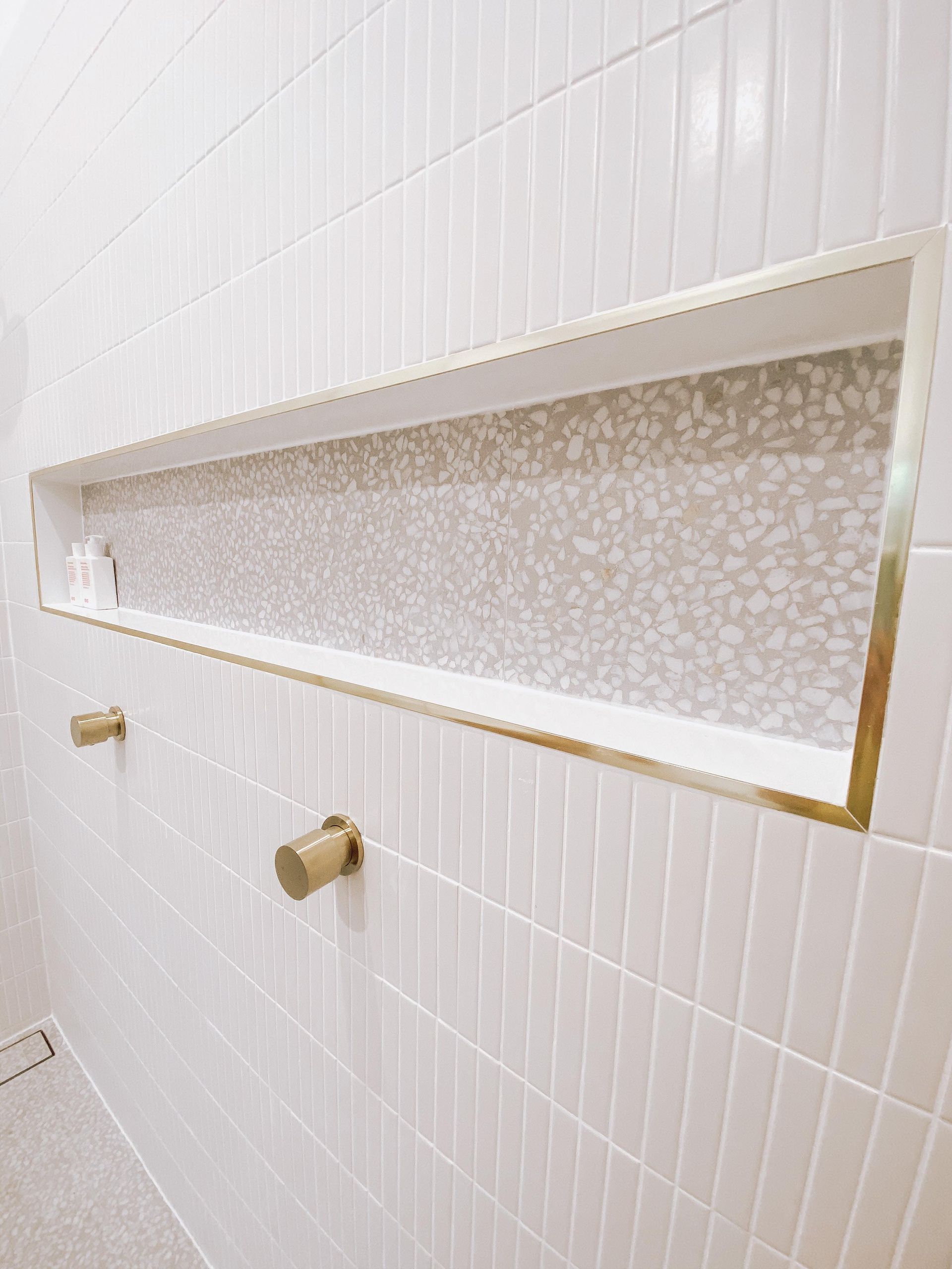 A shower niche in a bathroom with white tiles and gold trim.