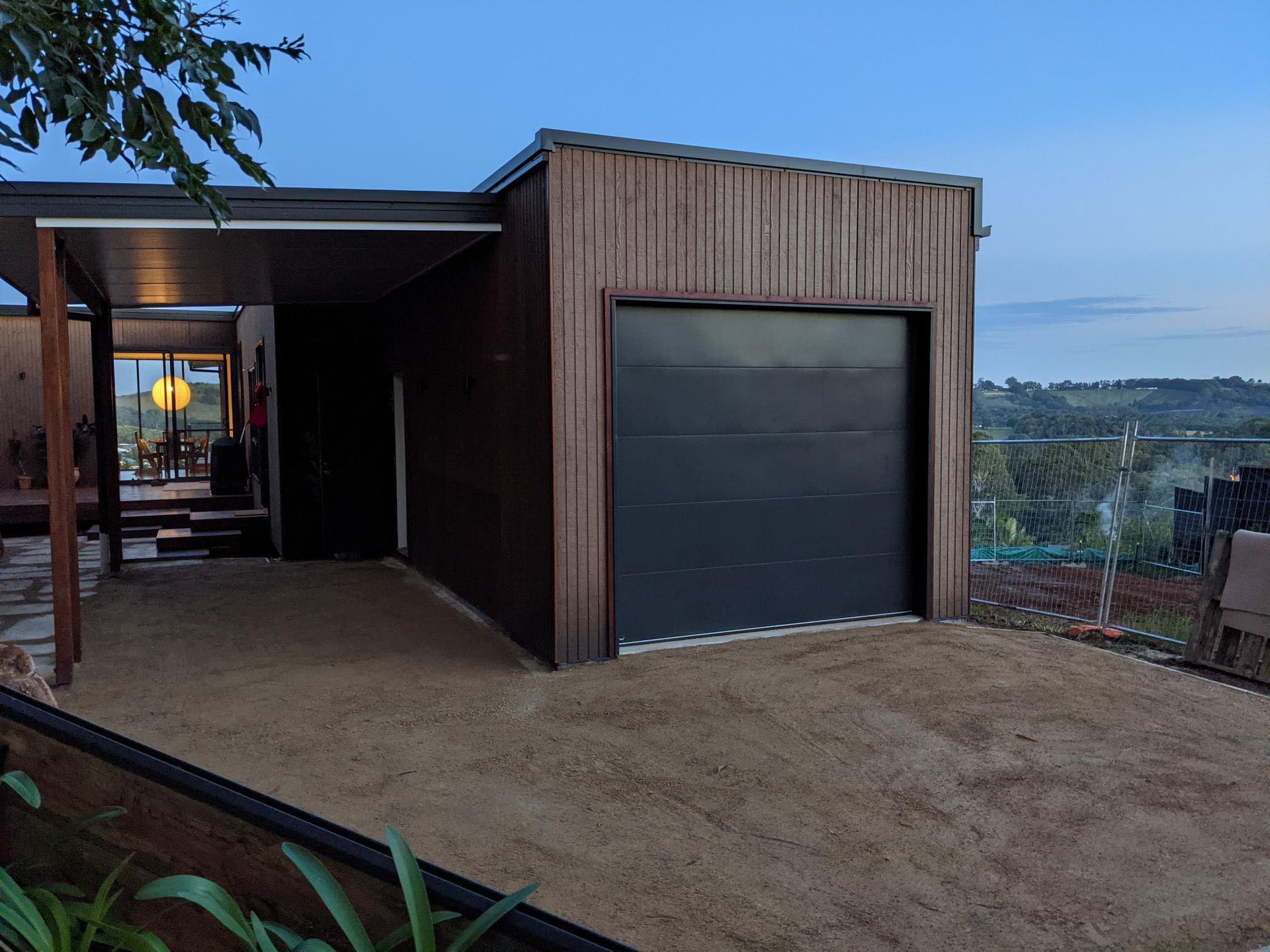 Garage with a dark gray door, next to a porch, in a light brown gravel yard. Overcast sky.