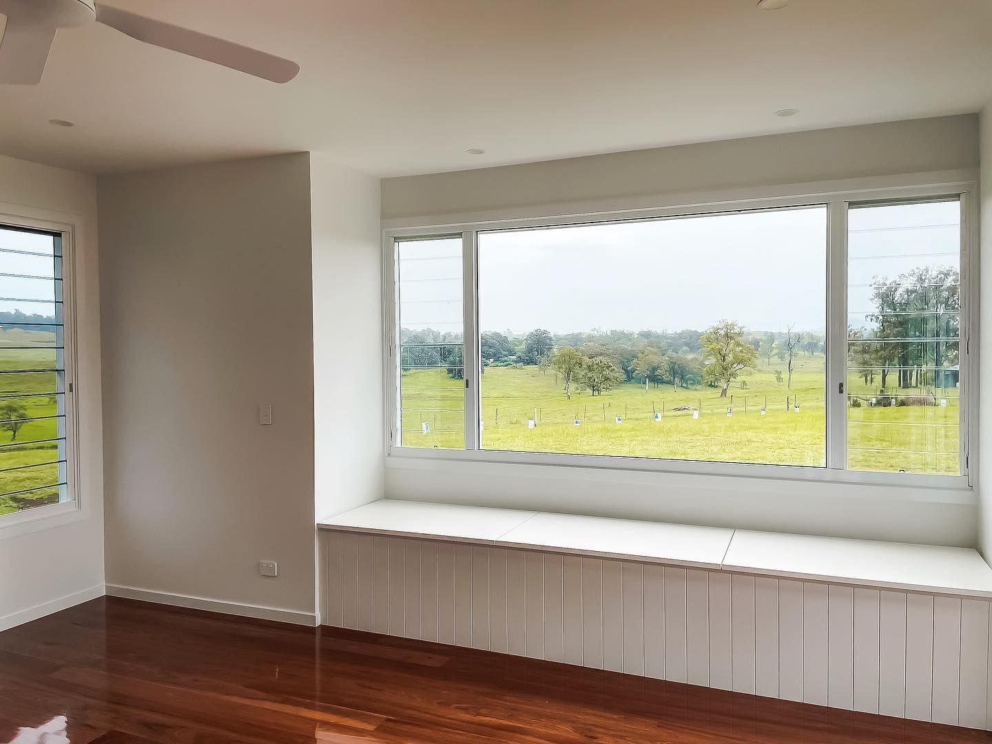 An empty room with a window seat and a ceiling fan.