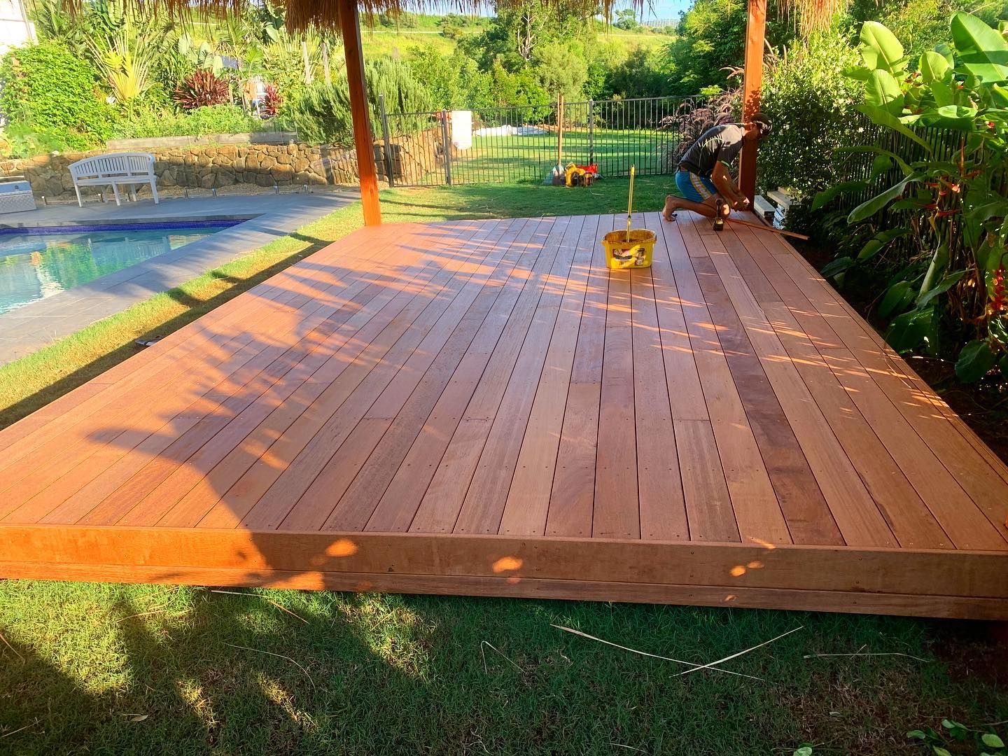A man is working on a wooden deck next to a pool.