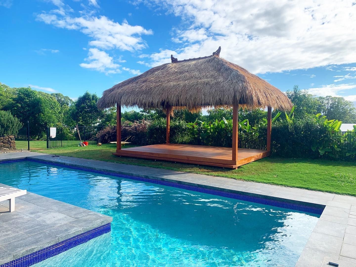 There is a thatched gazebo next to a swimming pool.