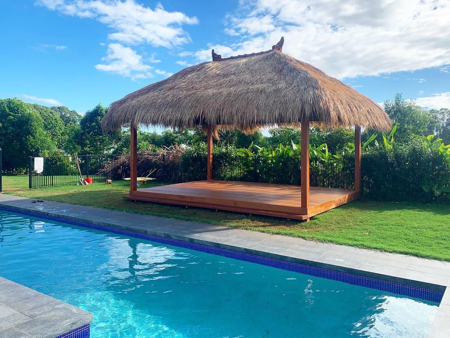 a thatched gazebo is sitting next to a swimming pool .