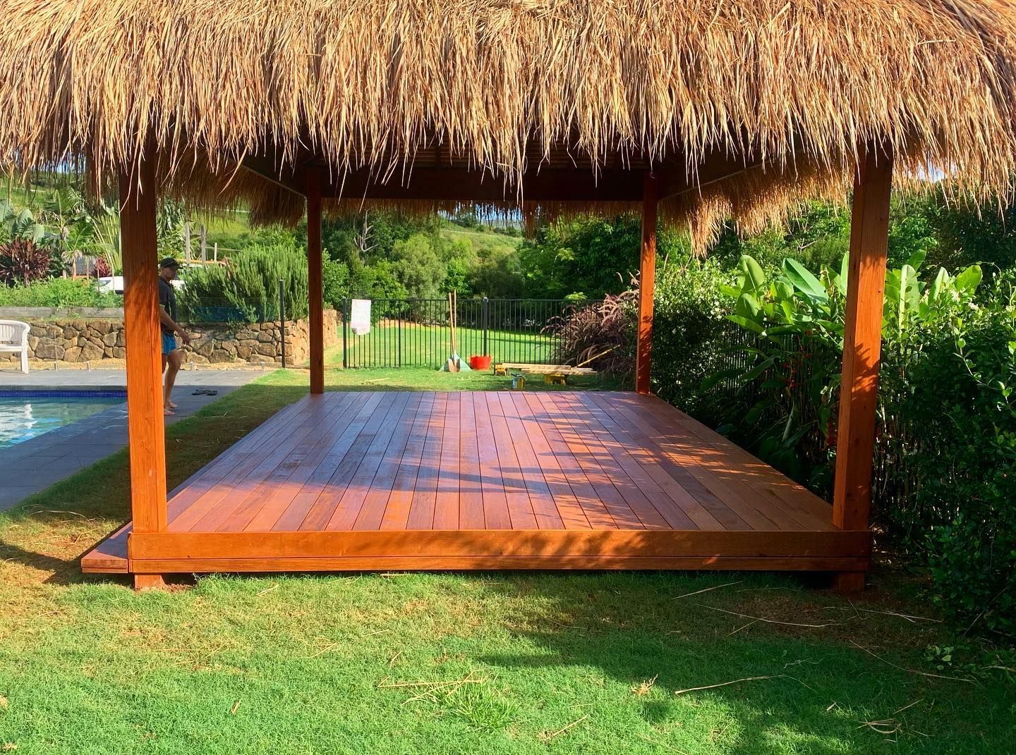 A wooden deck with a thatched roof next to a pool.
