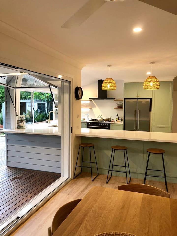 Kitchen with a bar, light green cabinets, and a counter with barstools. Indoor-outdoor access.