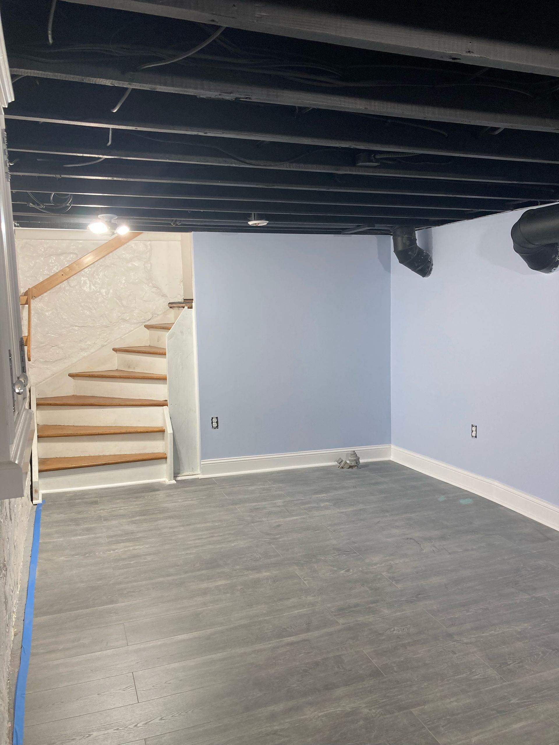 An empty basement with stairs and a black ceiling.